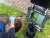Ein Techniker mit blauen Handschuhen führt ein Kamerakabel in einen geöffneten Kanalschacht